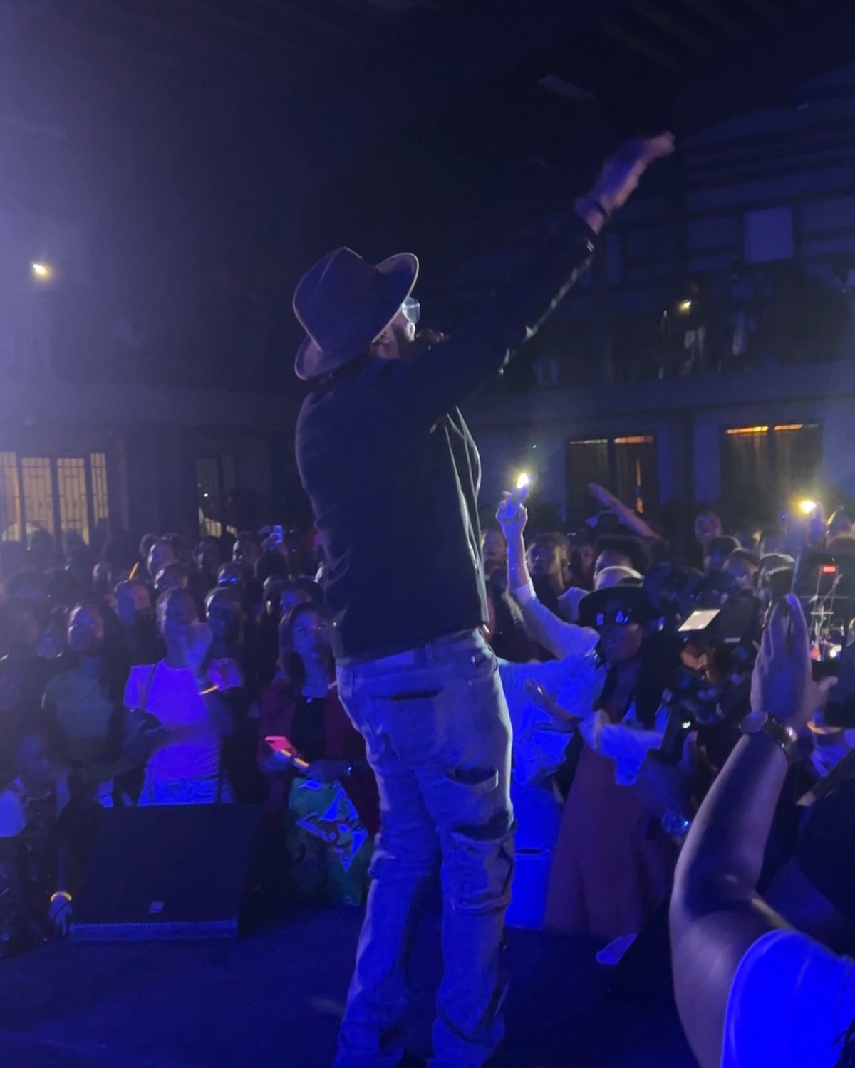 Kevin Downswell on stage, arm raised toward a packed crowd lit blue, phone lights and hands in the air