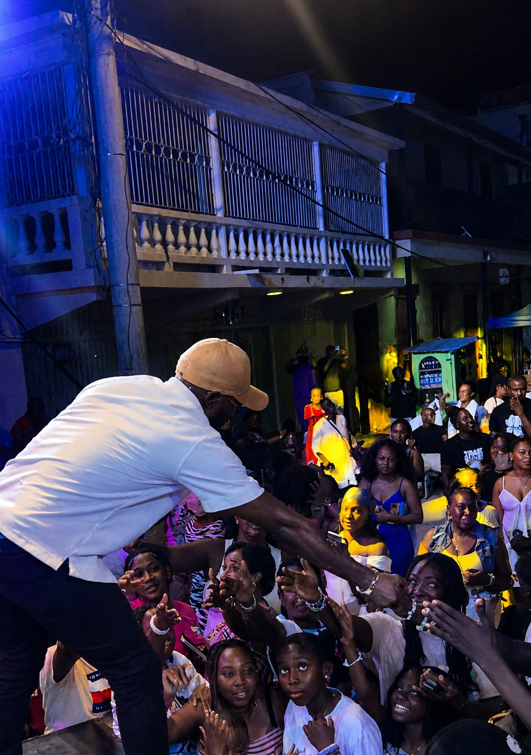 Kevin Downswell leaning from a stage at night to clasp hands with a crowd reaching toward him