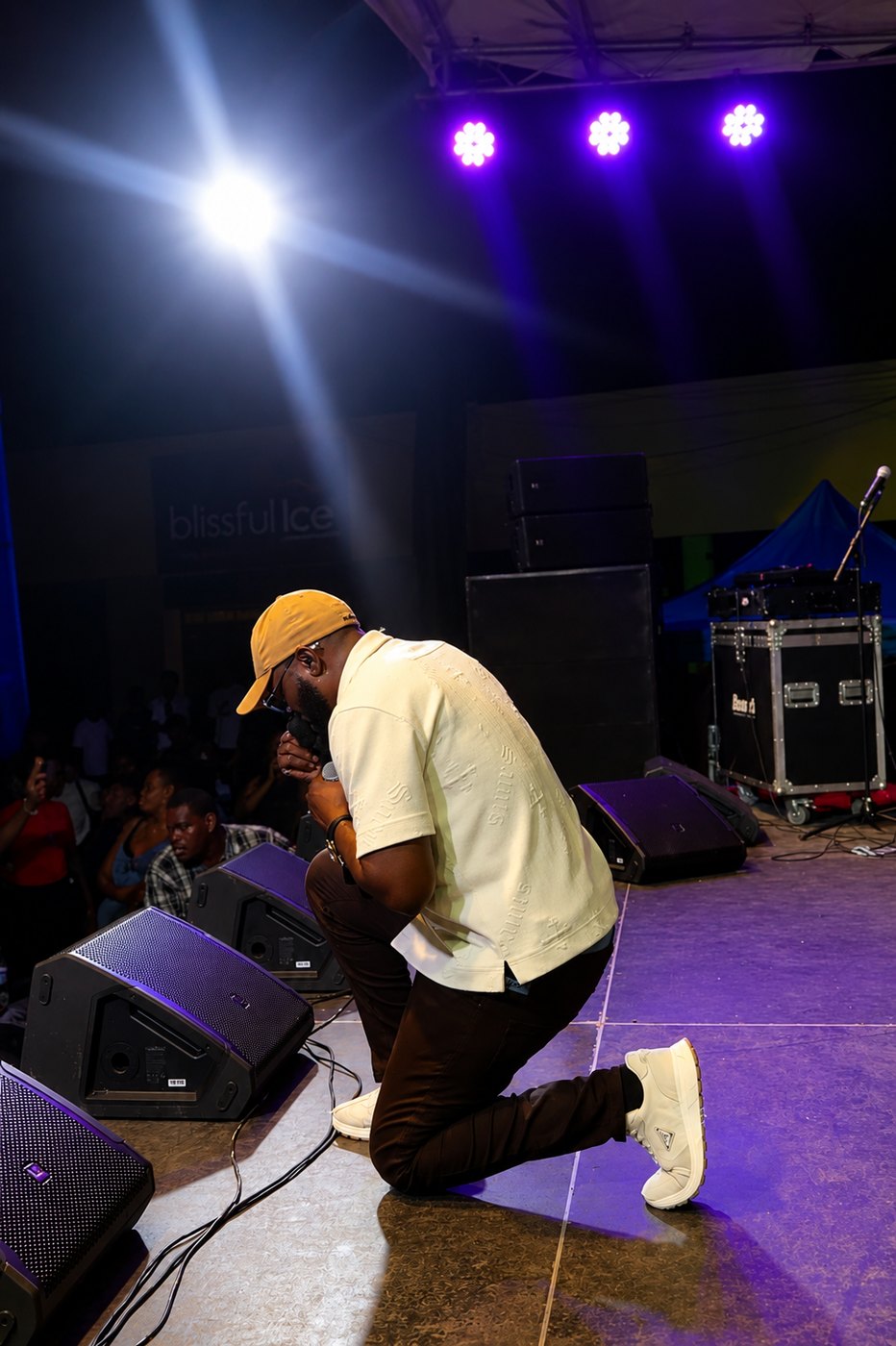 Kevin Downswell kneeling in prayer at the edge of a stage, microphone held to his face