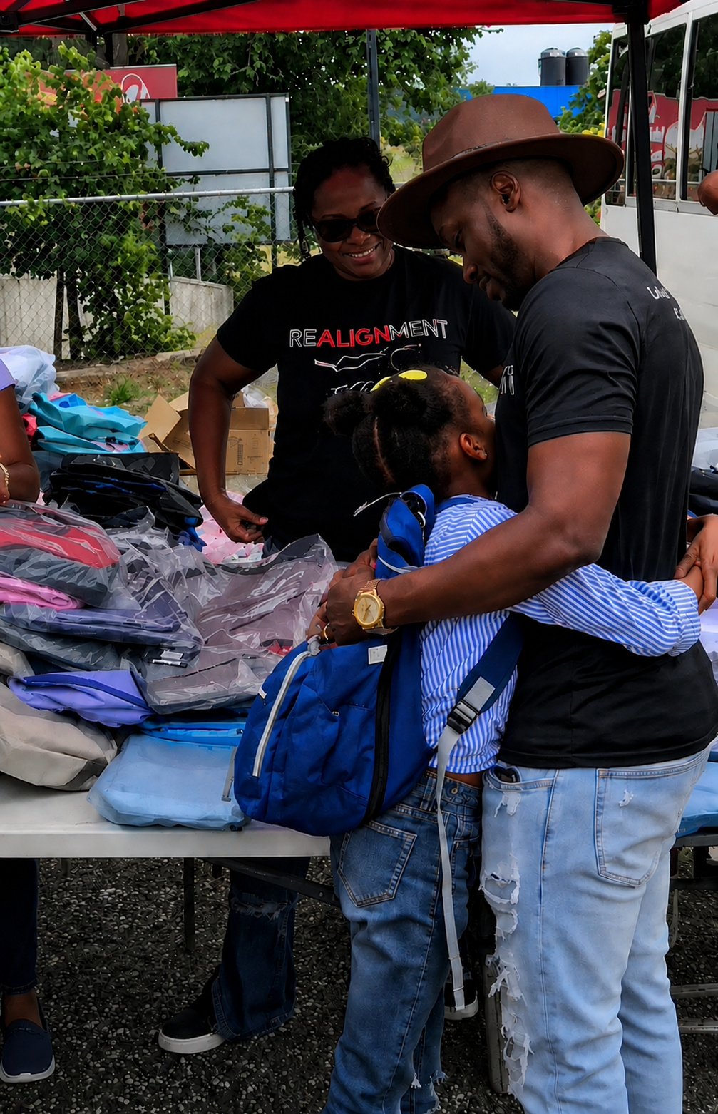 Kevin Downswell embracing a child at a Realignment Initiative outreach, a table of backpacks beside them