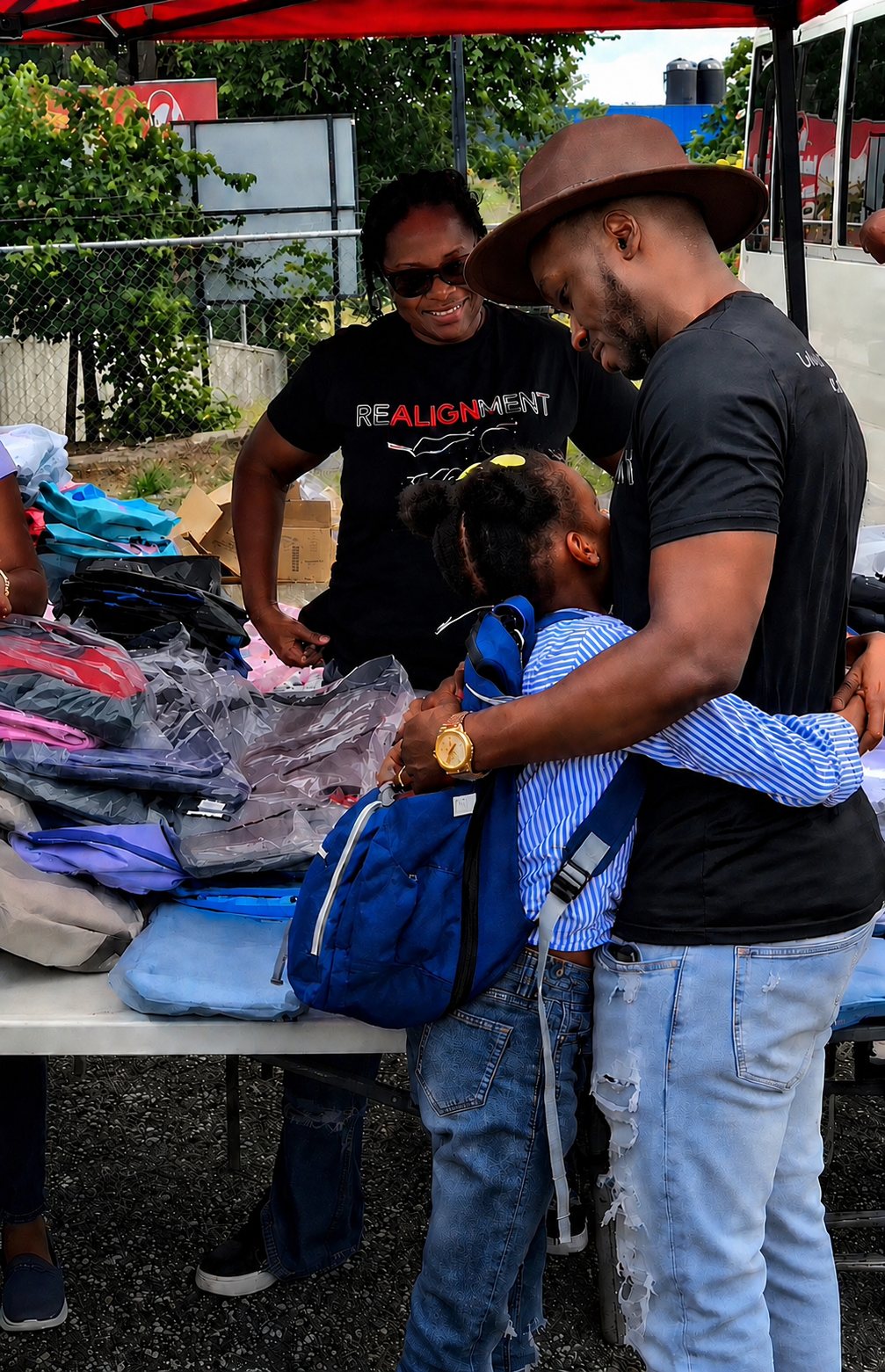 Kevin Downswell embracing a young girl with a new backpack at a roadside outreach table stacked with school supplies